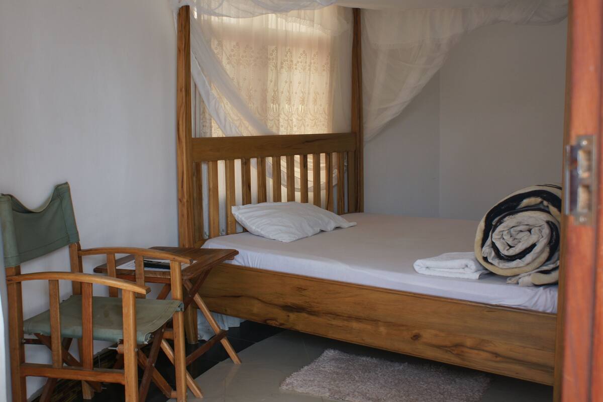 Un lit simple avec un cadre en bois, une chaise verte et un couvre-lit blanc.
