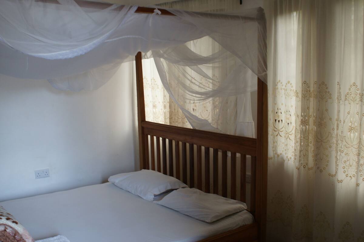 Un lit simple avec une tête de lit en bois, une literie blanche et un ciel de lit.