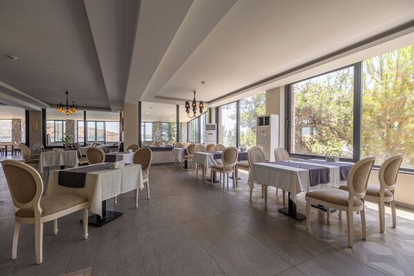 Un vaste espace dédié à la salle à manger, avec de nombreuses tables et chaises, de grandes fenêtres et un lustre moderne.