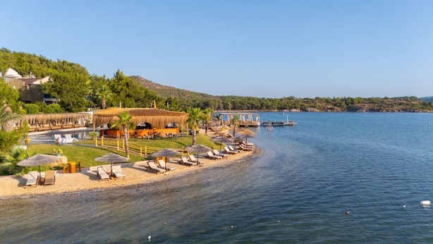 A coastal hotel with a beach area, lounge chairs, umbrellas, and a dock. - Khaja Beach Hotel (Ayvalik)
