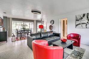 A modern living room with a black leather sofa, red chairs, a dining area with a table and chairs, and a large abstract painting on the wall. - Walk to FIT Campus! Pet-Friendly Home in Melbourne (Melbourne)