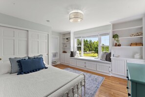 A bedroom with a bed, built-in shelving, a window seat, and a view of greenery. - Spacious Family Getaway on Apple Orchard in Hugo! (Hugo)