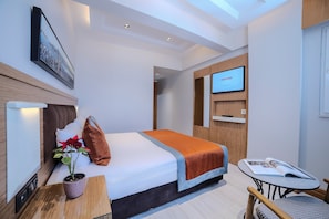 A modern hotel room with a bed, a small table, a TV, and a potted plant.