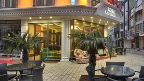 Hotellin edessä on kyltti, jossa lukee ”HOTEL RESIPASA”. Ulkona on terassialue, jossa on pöytiä ja tuoleja, ja liikkeen ikkunassa on kyltti, jossa mainostetaan alusvaatteita ja sukkia.