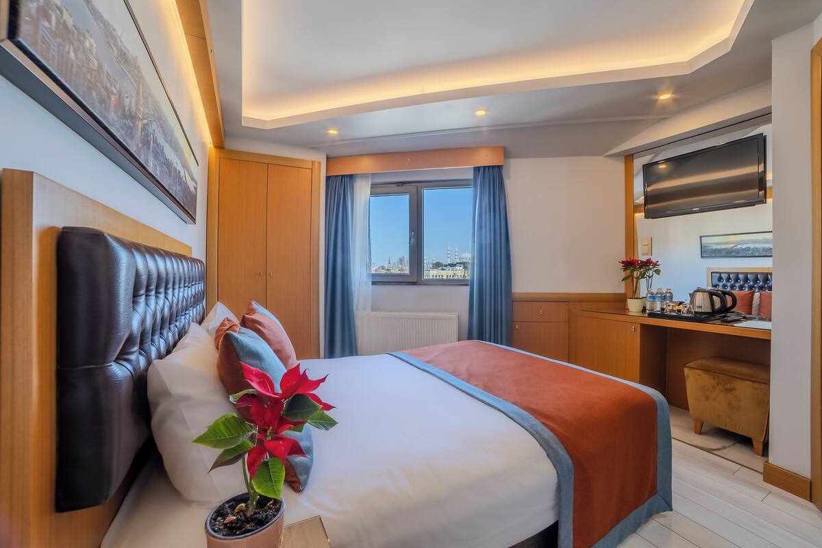 Una habitación de hotel moderna con una cama grande, vistas a la ciudad, un televisor de pantalla plana y una kitchenette.