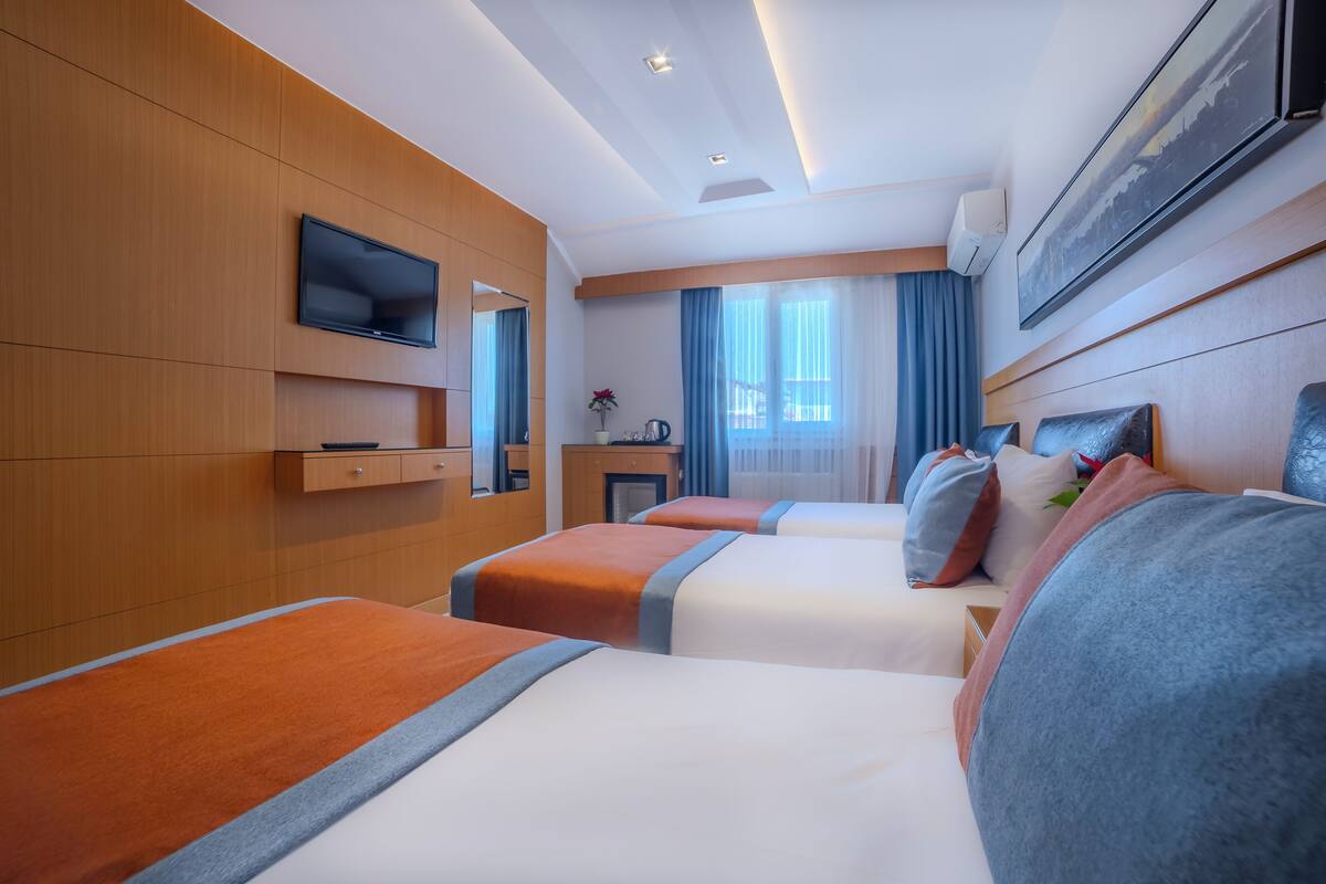 Habitación de hotel con dos camas, televisión, escritorio y ventana con cortinas.