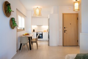 A modern kitchen with white cabinets, a dining table with chairs, and a wooden door. - 1-Bedroom Contemporary Coastal Suite with Outdoor Hot Tub And Private Parking (Rethymno Town)
