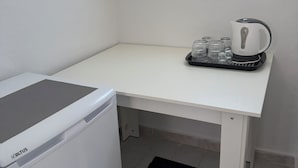 A compact room with a washing machine, a small table with a kettle and glasses, and a window. - Raeti Fira Residence (Santorini)