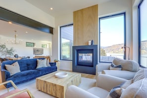 Ein modernes Wohnzimmer mit Kamin, großen Fenstern und einem blauen Sofa.