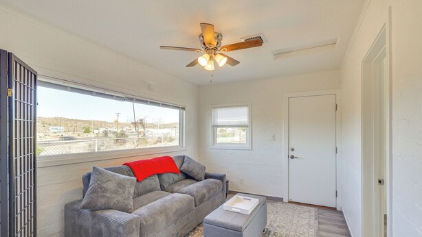 A room with a grey sofa, a red throw, a ceiling fan, and a view through a window. - Route 66 Roadtripper Retreat w/ Private Backyard (Kingman)
