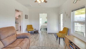 A spacious living area with a ceiling fan, a sofa, two armchairs, a bookshelf, and a view through a window. - Route 66 Roadtripper Retreat w/ Private Backyard (Kingman)