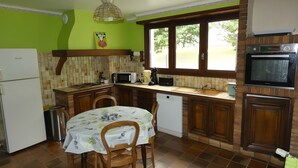 Angolo cottura compatto con tavolo, sedie, frigorifero, microonde, lavandino e finestra vista all'esterno.