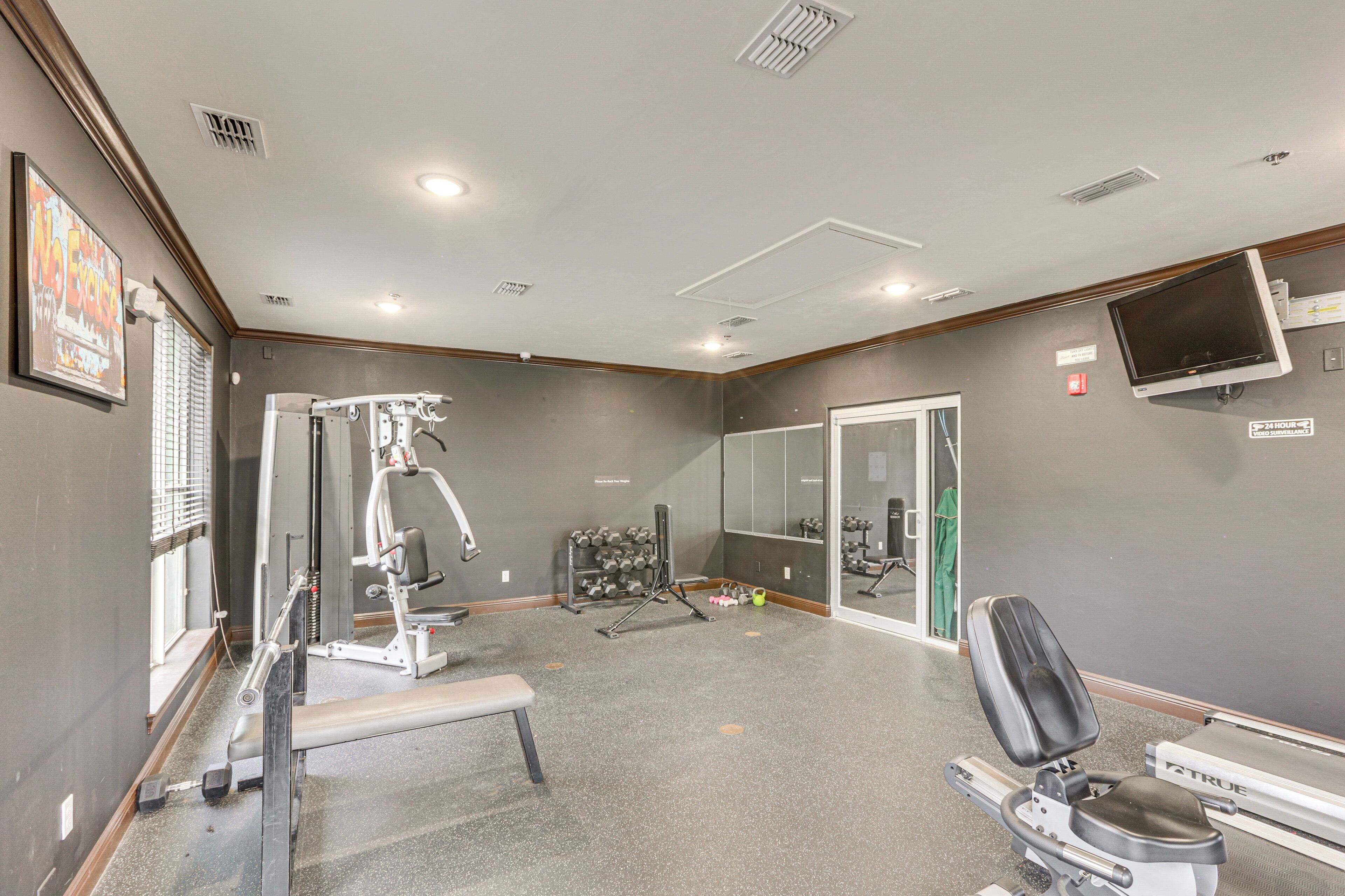Ein Fitnessraum mit Trainingsgeräten, einer Bank und einer Spiegelwand.
