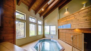 Un bain à remous dans un chalet en bois doté de grandes fenêtres et d’un plafond en bois.