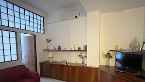 Ein Wohnzimmer mit einer Couch, einem Couchtisch, einem Fernseher, einem Bücherregal und einem großen Fenster.