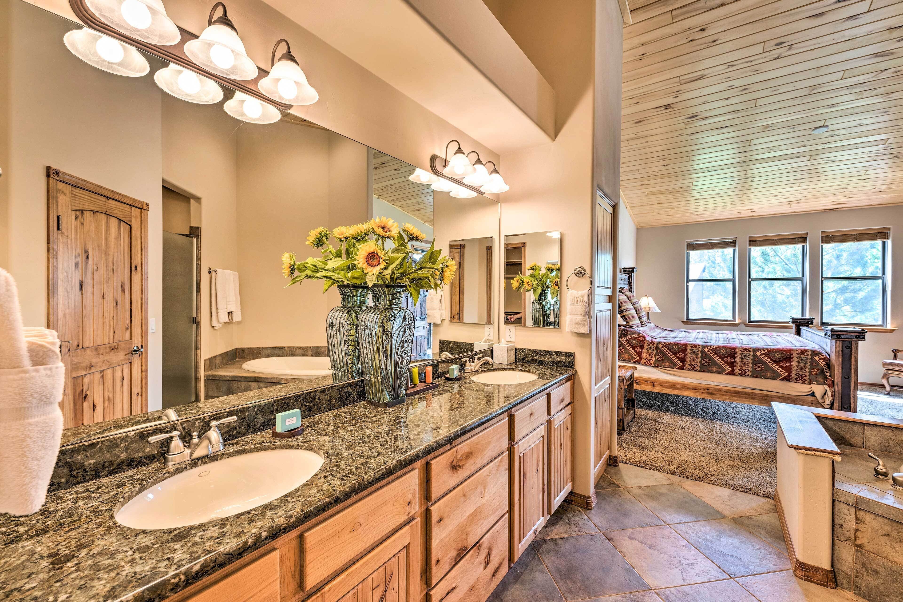 A spacious bathroom with granite countertops, a large mirror, and a wooden door.