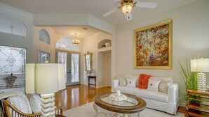 A spacious living room with a white sofa, a round coffee table, and a large painting on the wall. - Gated Home w/ Pool, On-Site Golf in Port Charlotte (Port Charlotte)