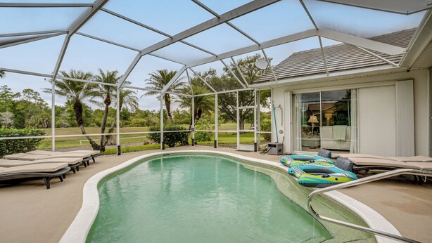 A covered swimming pool with lounge chairs and inflatable toys, surrounded by palm trees and a house. - Gated Home w/ Pool, On-Site Golf in Port Charlotte (Port Charlotte)