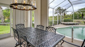 A covered outdoor area with a pool, a table with chairs, and a hanging light fixture. - Gated Home w/ Pool, On-Site Golf in Port Charlotte (Port Charlotte)