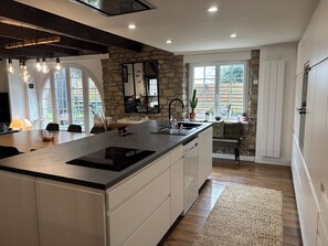 A modern kitchen with a large island, stone accent walls, and a view to the outside. - Character house near the sea (Ploemeur)