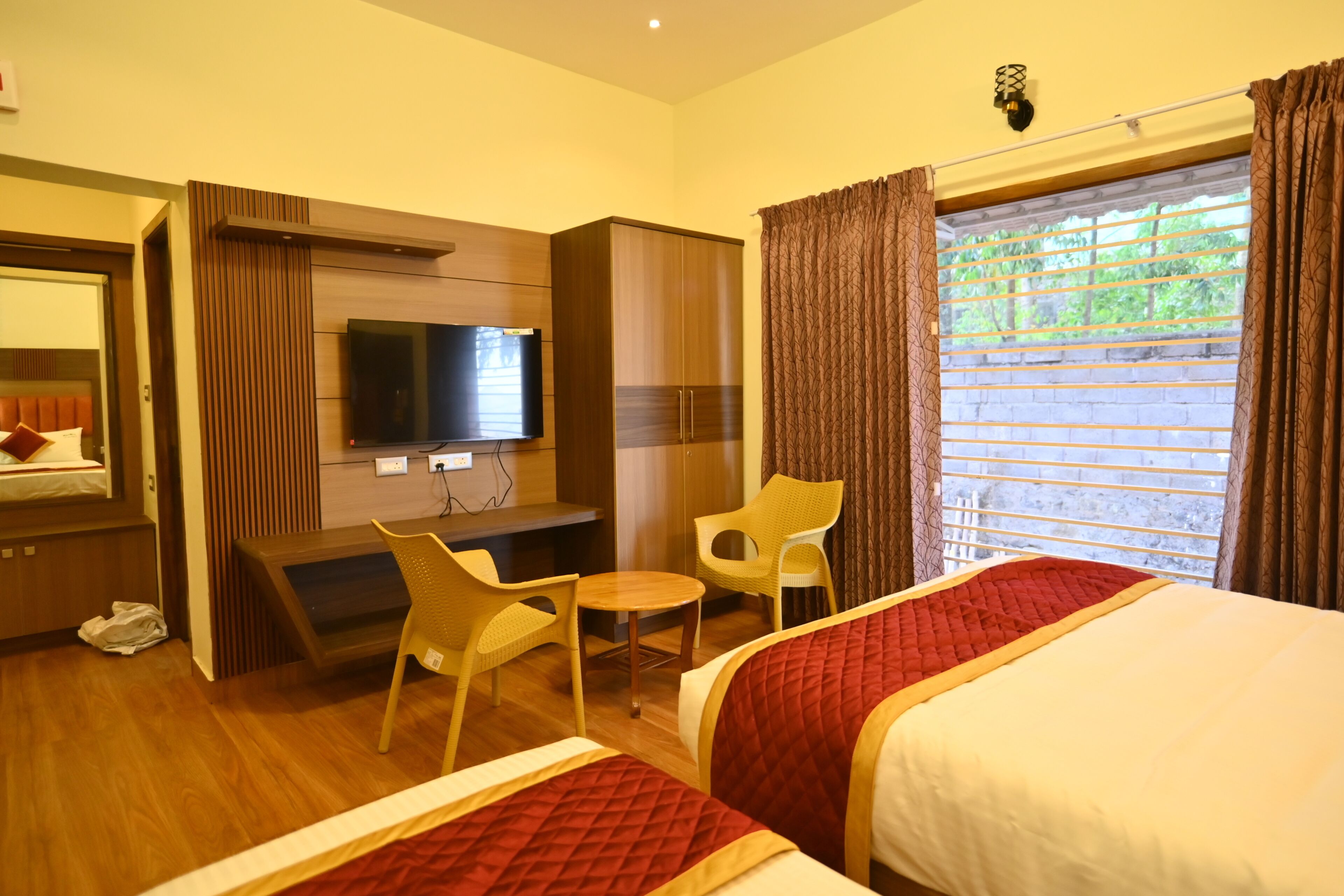 Habitación de hotel con cama, televisor, escritorio, silla y ventana con cortinas.