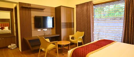 Habitación de hotel con cama, televisor, escritorio, silla y ventana con cortinas.