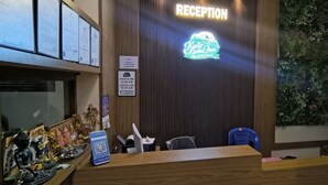 A reception desk with a neon sign, a blue chair, a QR code, and a wall with a vertical garden. - KULIR KODAI INN  (Kodaikanal)