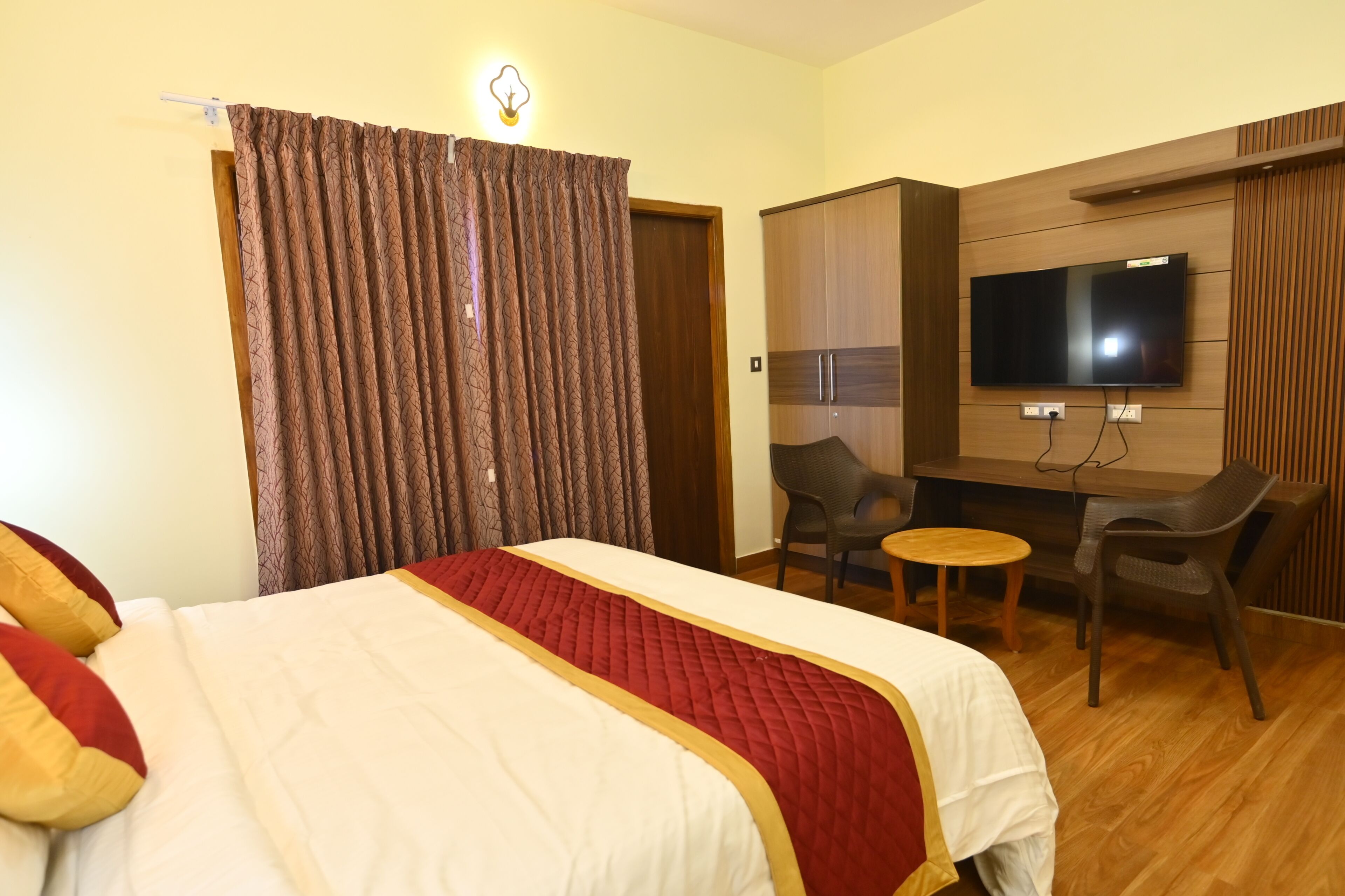 A hotel room with a bed, curtains, a TV, a desk, and two chairs.