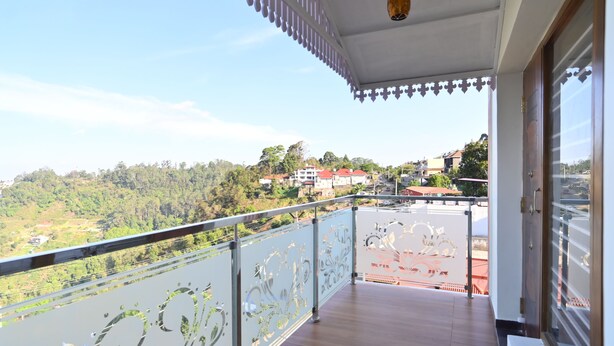 A balcony with a view of a hilly landscape and buildings. - KULIR KODAI INN  (Kodaikanal)