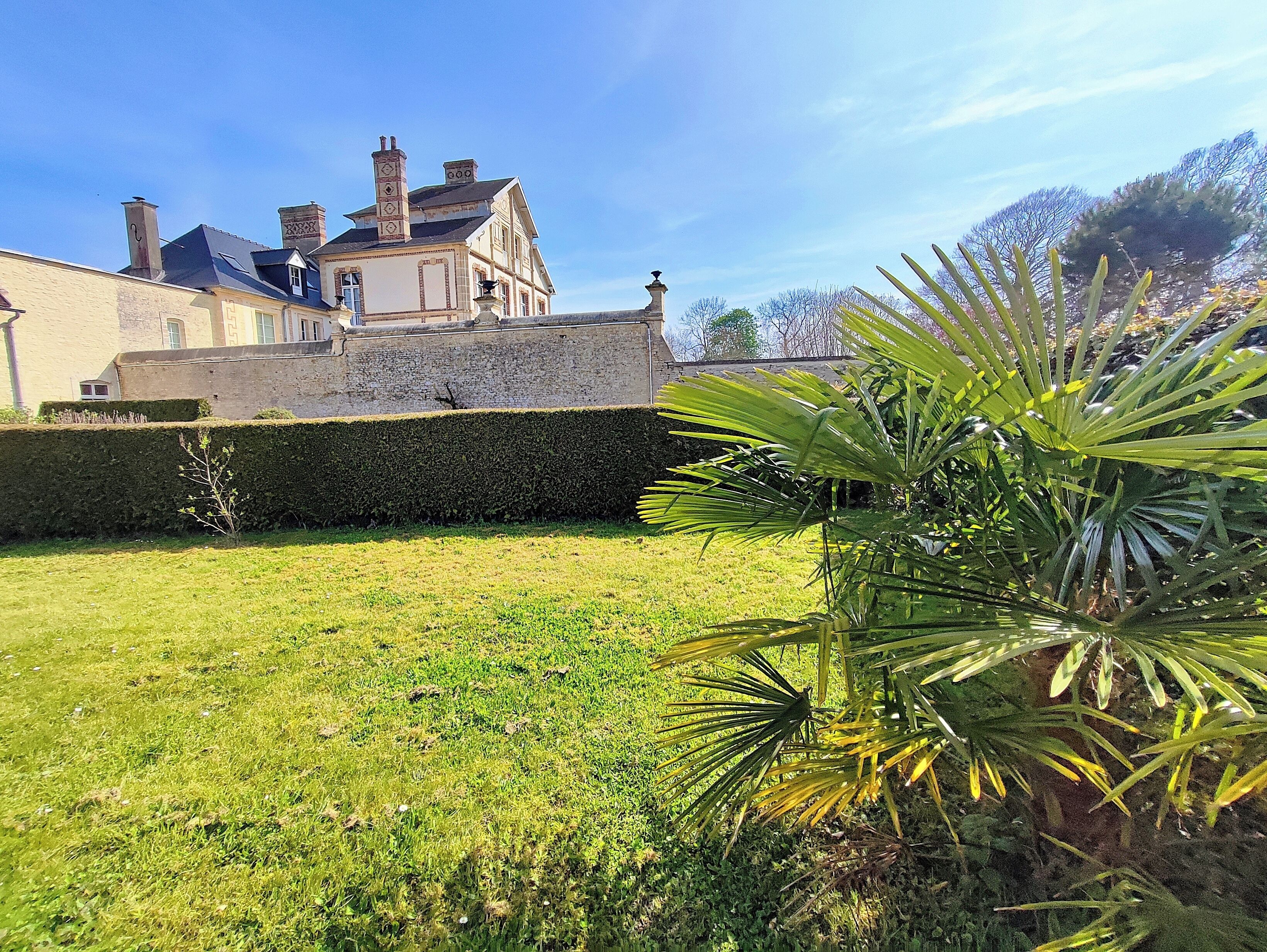 Un grand bâtiment à la façade en pierre, avec une pelouse bien entretenue et un palmier.