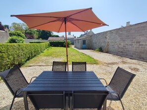 En terrasse med et bord, stole, en parasol og en hæk.