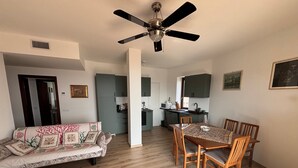 Ein Wohnzimmer mit einer Couch, einem Esstisch, Stühlen, einem Deckenventilator und einer Küche im Hintergrund.
