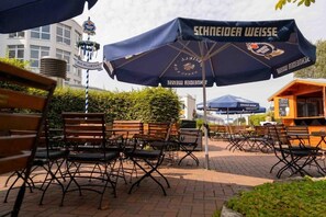 Outdoor seating with umbrellas, a beer garden sign, and a building in the background. - DLRG Tagungszentrum Hotel Delphin (Bad Nenndorf)