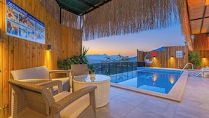 Área de piscina com mobiliário de vime, piscina de vidro e vista para as montanhas.