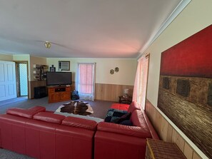 A living room with a red sofa, a television, a wooden cabinet, and a large abstract painting on the wall. - Cosy Beach House, 10 mins walk to beach, pet friendly (Venus Bay)