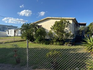 A single-story house with a front porch, a fenced yard, and a small staircase leading to a deck. - Cosy Beach House, 10 mins walk to beach, pet friendly (Venus Bay)