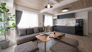 Moderni olohuone, jossa on sohva, ruokapöytä sekä keittiöalue, jossa on kaappeja ja kodinkoneita.
