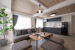 A modern living room with a sofa, a dining table, and a kitchen area with cabinets and appliances. - Shinjuku 6-chome City Stay (Tokyo)