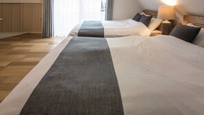 Hotellihuone, jossa on kaksi sänkyä, kattovalaisin, yöpöytä lampun kanssa ja ikkuna, jossa on verhot.