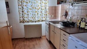 Een keuken met houten vloeren, een radiator, een spoelbak, kasten en een koelkast.