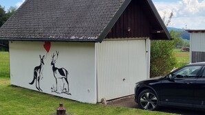 Een gebouw met een schuin dak, een muurschildering van kangoeroes en een hart, en een geparkeerde auto in de buurt.