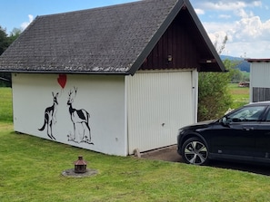 A building with a sloped roof, a mural of kangaroos and a heart, and a car parked nearby.