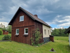 A two-story wooden house with a sloped roof, a small front porch, and a fenced yard.