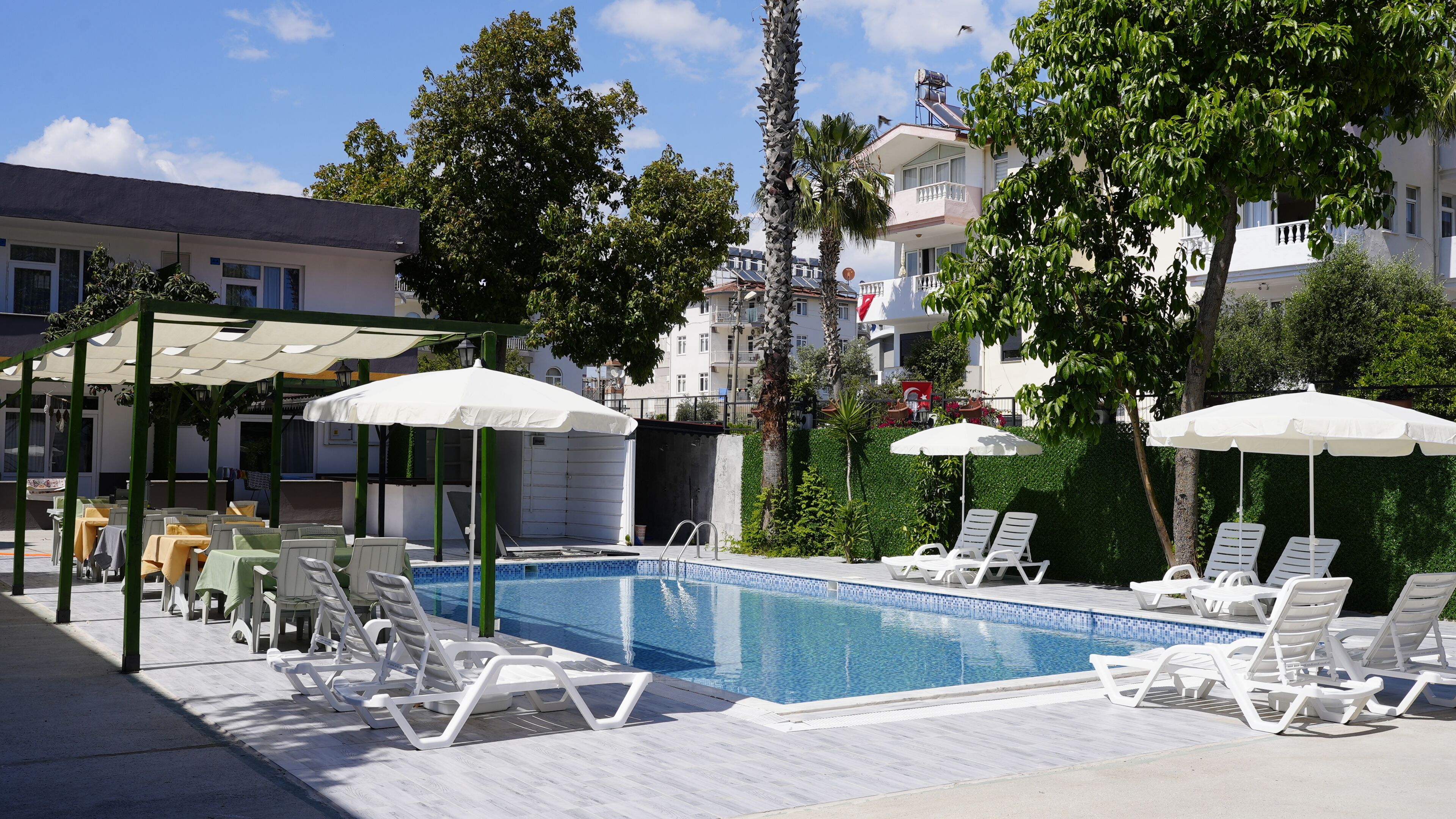 Ein Poolbereich mit Liegestühlen und Sonnenschirmen, umgeben von Grünflächen und Gebäuden.