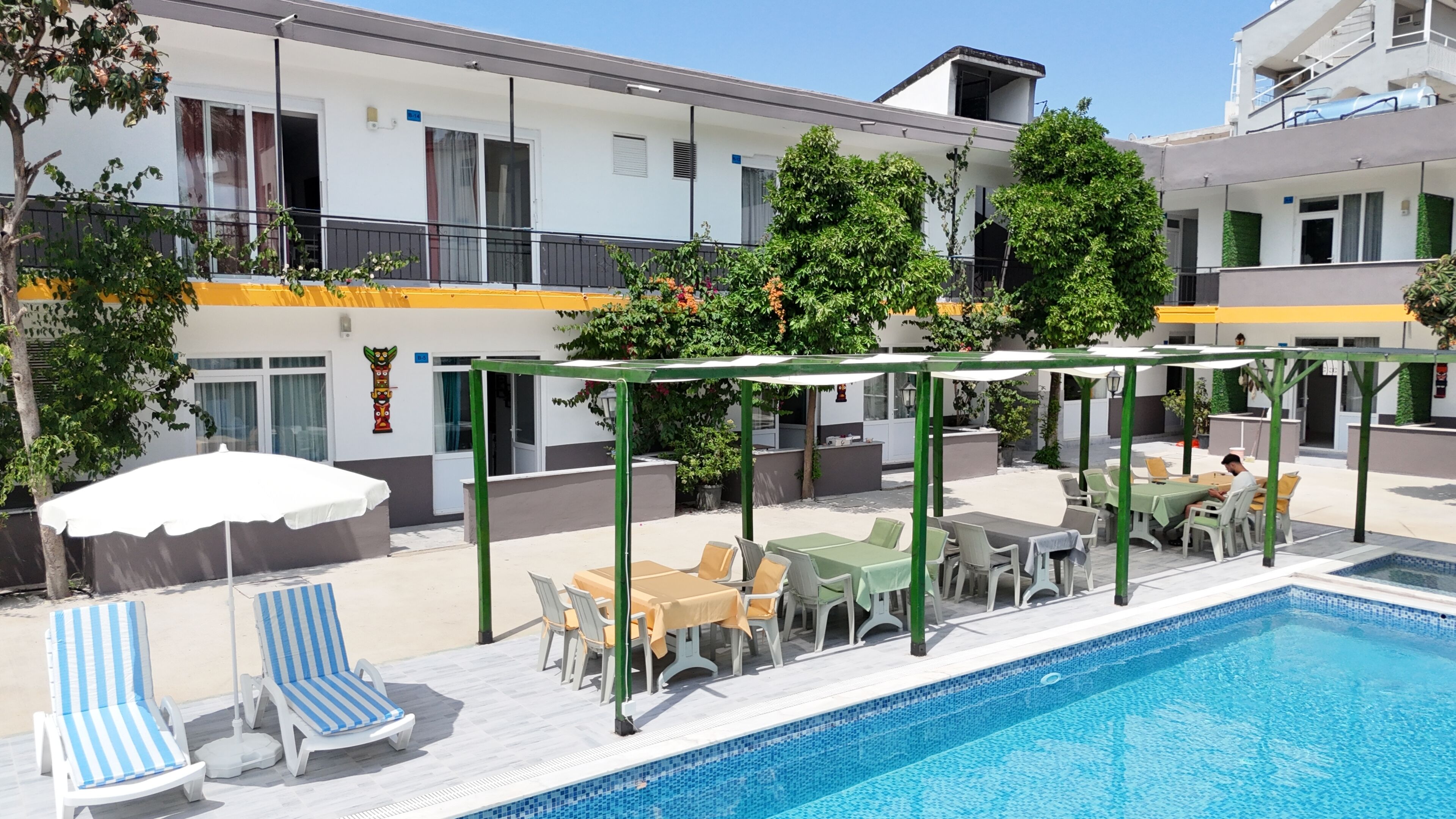 A swimming pool with lounge chairs and tables, surrounded by a covered patio area.