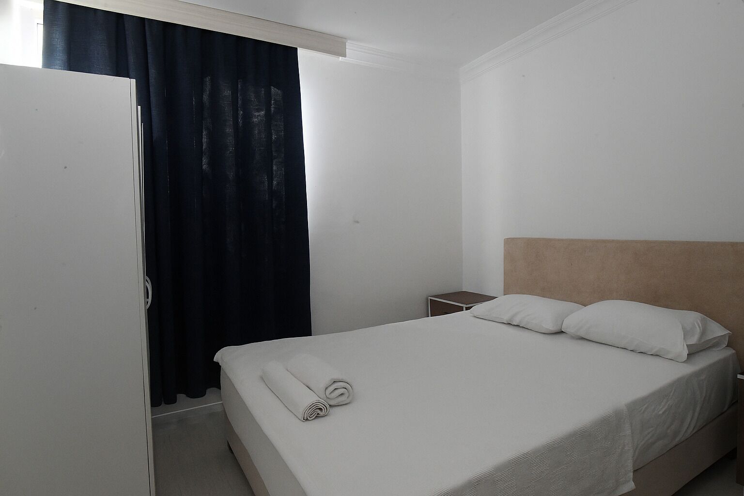 Quarto de hotel com cama, mesa de cabeceira, guarda-roupa e janela com cortinas.
