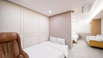 A hotel room with a large bed, a sitting area with a chair, a small table, and a wardrobe.