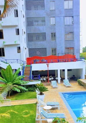 A hotel with a pool, lounge chairs, and a covered outdoor area with tables and chairs. - Luxurious 2 Bedroom in Kilimani With Scenic Views and Modern Amenities (Nairobi)