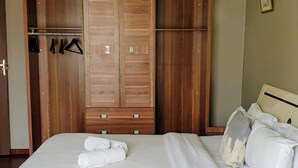 Quarto com cama, guarda-roupa de madeira e mesa de cabeceira.