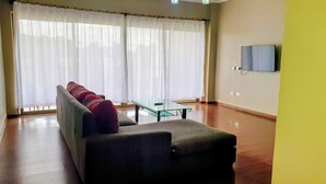Een woonkamer met een bank, een glazen salontafel en een aan de muur bevestigde televisie.